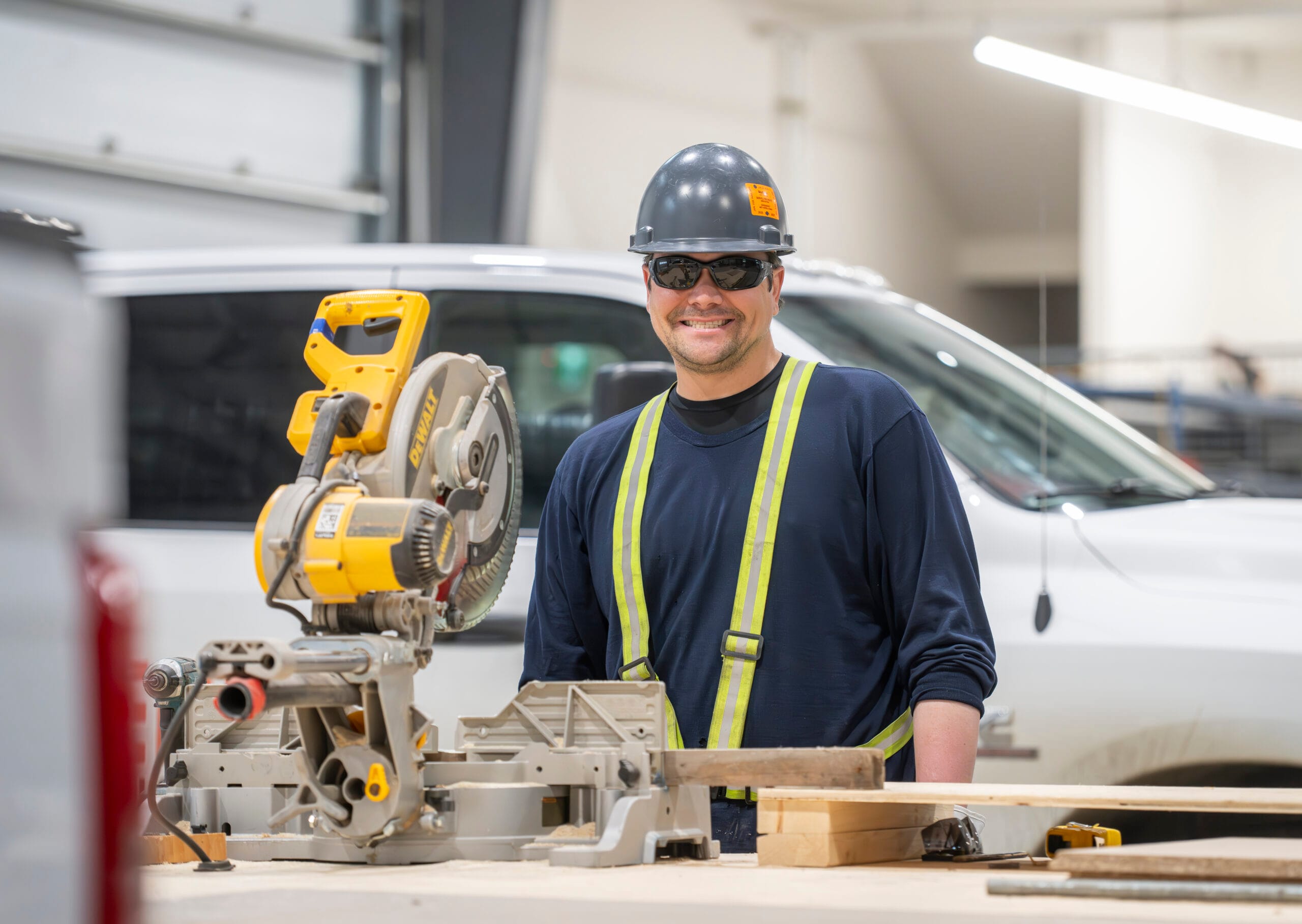 A construction worker cuts wood on a workbench with a chop saw.