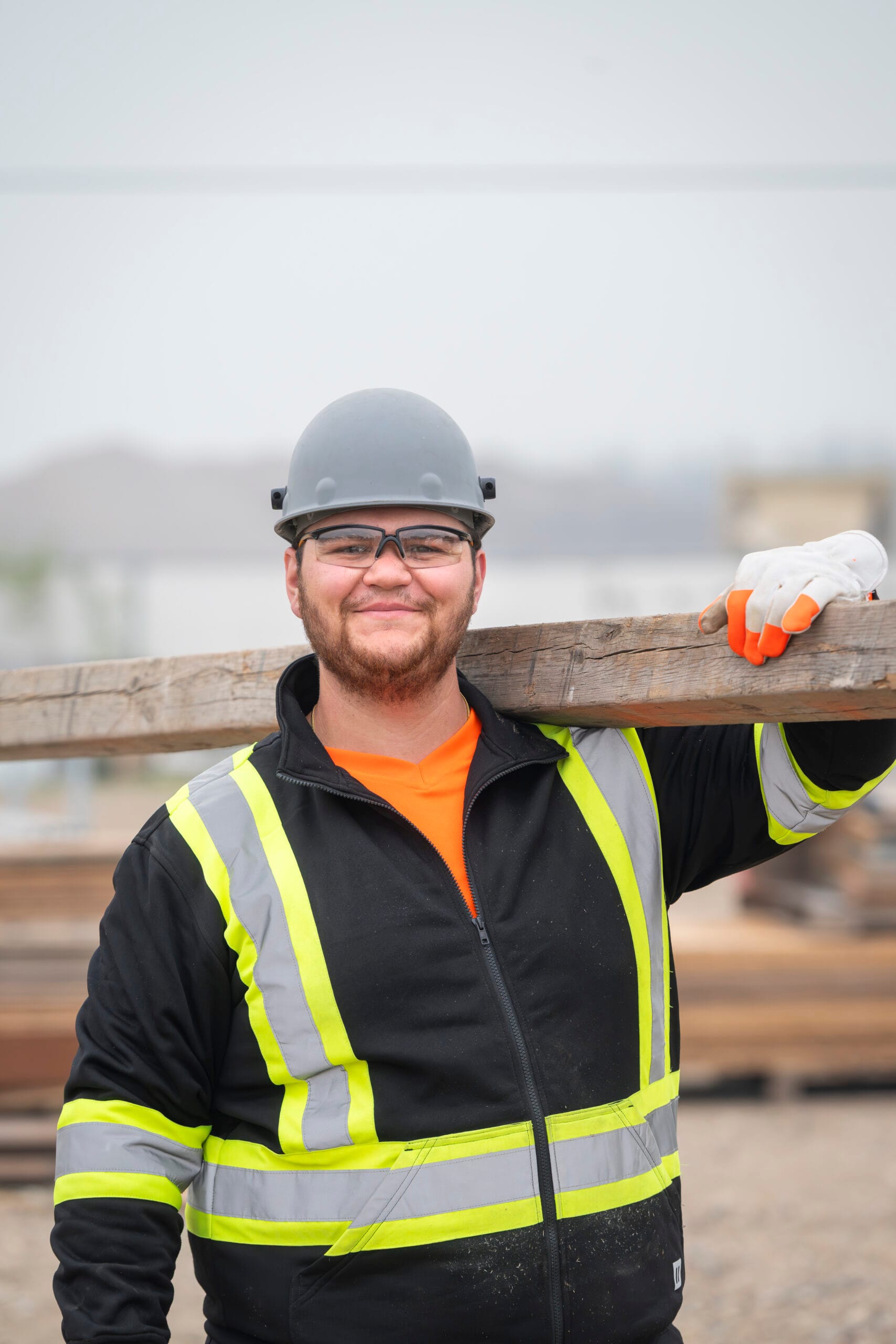 Man holding a piece of wood on his shoulder at a construction site.