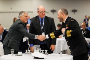 Three professionals shake hands at the Saskatchewan Aerospace and Defence Forum, including a Canadian Armed Forces member in uniform, highlighting industry and military collaboration in Saskatchewan’s aerospace and defence sector.
