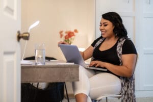Woman working from home, sitting at a desk and using a laptop, focused on her work.