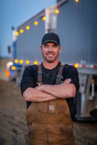 Saskatchewan Supply Chain Week graphic featuring a transport truck driver standing beside a semi-truck.